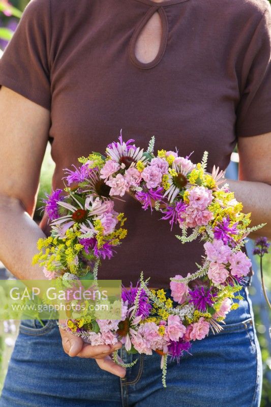Woman holding summer wreath made of mostly pink flowers including Echinacea, Rosa, Fennel, Monarda and Veronicastrum.