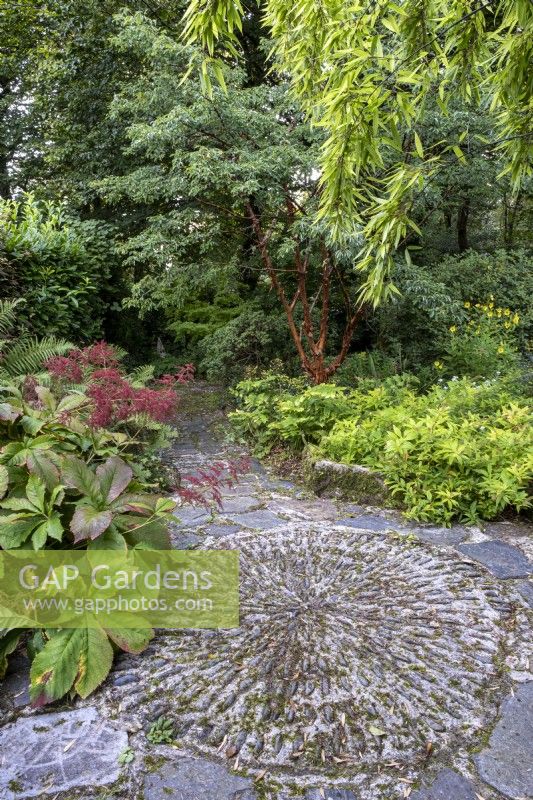 Decorative cobbled circular area, in a shady and lush autumnal garden