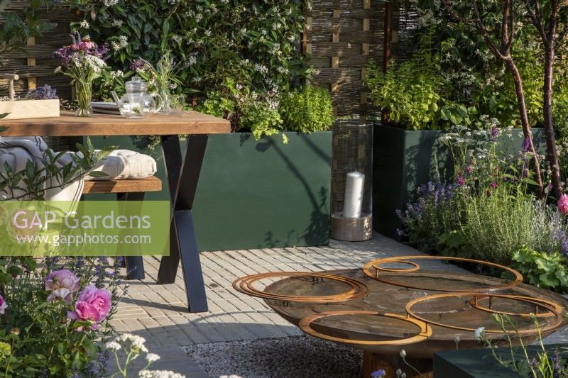 Reclaimed circular corten steel water feature with rusty hoops - green metal raised bed containers planted with Trachelospermum jasminoides - Star jasmine