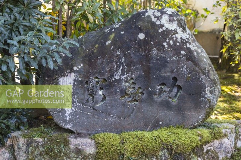 Stone with inscription in Japanese sitting on moss covered stone surface. 