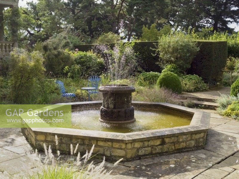 Urn shaped fountain and octagonal water feature in paved area of garden
