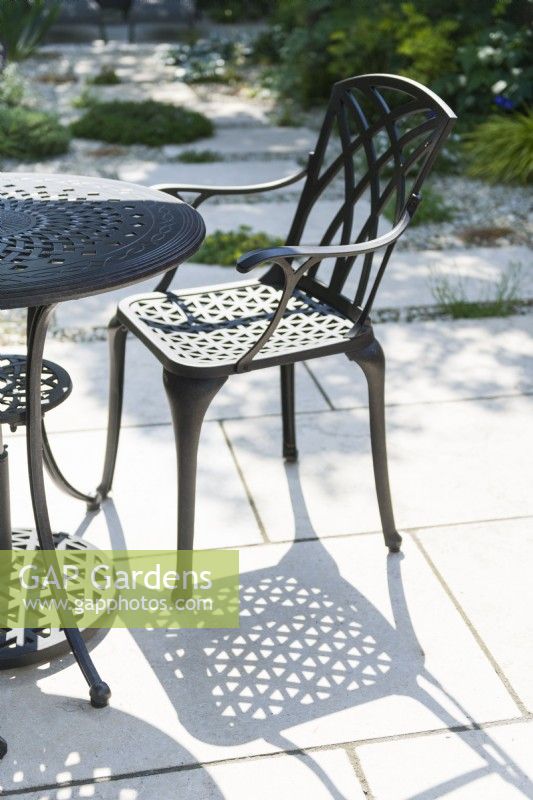 Aluminium alloy garden table and chair casting shadows on limestone paving in summer. June.