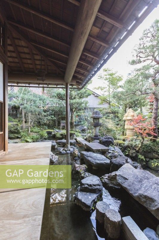 Covered veranda at the back of the house with view into the garden. Rocks placed as stepping stones across water with two stone lanterns or Ishidoro. 