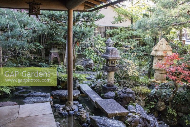 Covered veranda at the back of the house with view into the garden. Rocks placed as stepping stones across water with two stone lanterns or Ishidoro. Straw wrapped fragile stone ornaments as protection against frost.