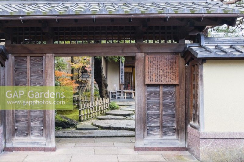 View into the entrance to the house and garden with notices in Japanese and wide stepping stones inside entrance and a low bamboo railing.