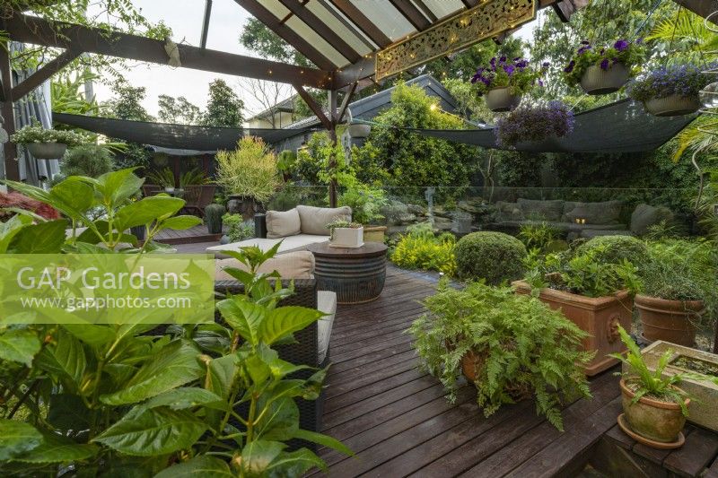 Balinese style outdoor covered patio with lounges, hanging baskets and potted plants.