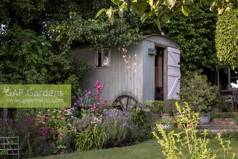 Shepherd's hut in summer garden, hidden amongst shady mature trees