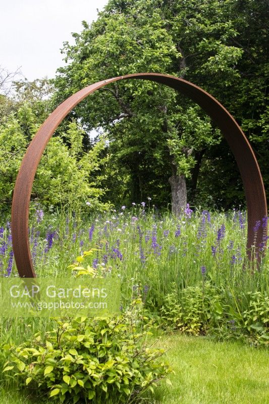 A Corten steel moon gate marks the entrance to a perennial wildflower meadow.