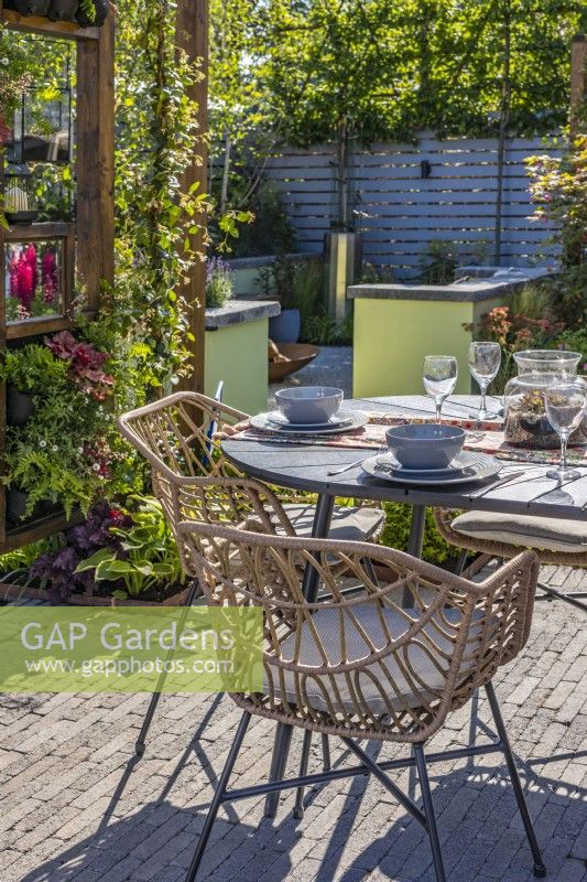 The dining area with a table and chairs is surrounded by a wooden pergola with Trachelospermum jasminoides - Star jasmine., heucheras and ferns. Corner with a firepit at the back. Designer: Colm Carty
