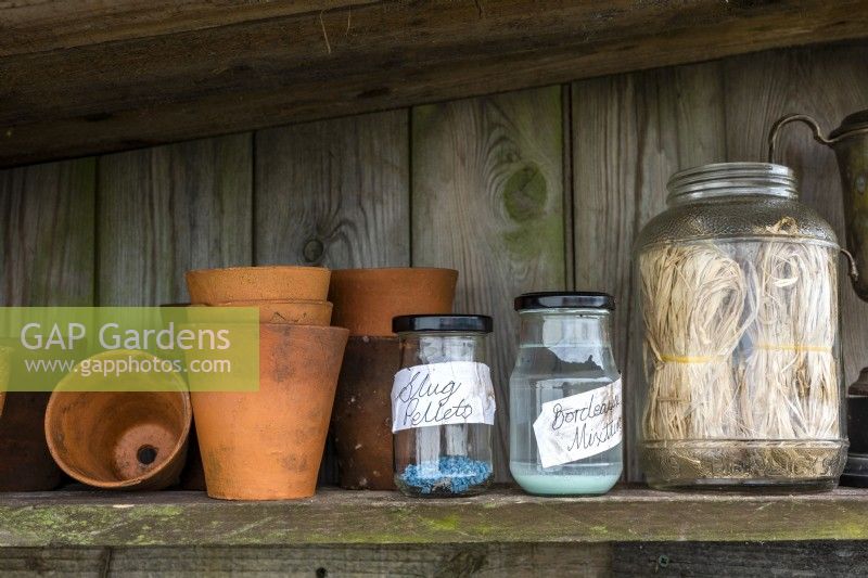 Clay pots, jars with slug pellets and bordeaux mixture and strings placed on a wooden shelf 