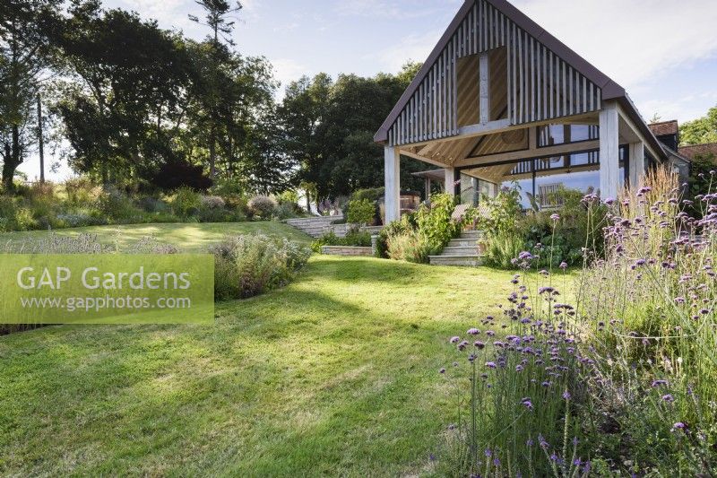 Country garden in July with beds of herbaceous perennials around a contemporary house extension