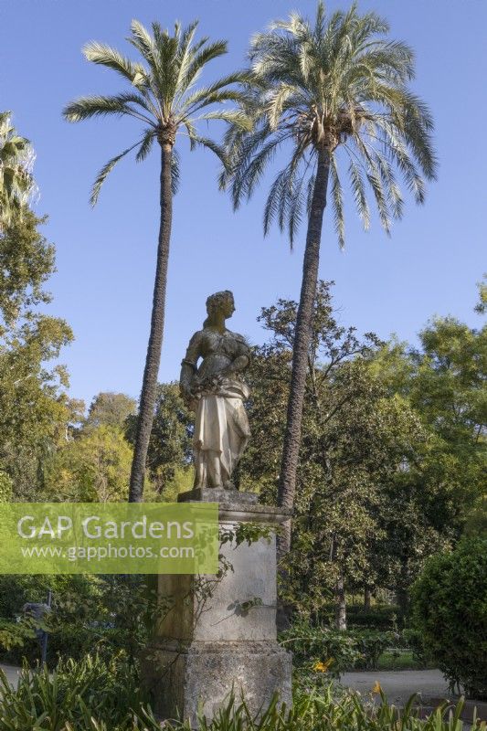 A figurative statue of a woman on a stone plinth. Parque de Maria Luisa, Seville, Spain. September