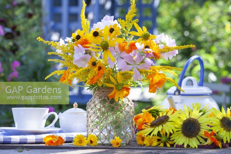 Summer flower bouquet with Rudbeckia, Tropaeolum majus, Solidago and Malva in a glass jar decorated with twine.