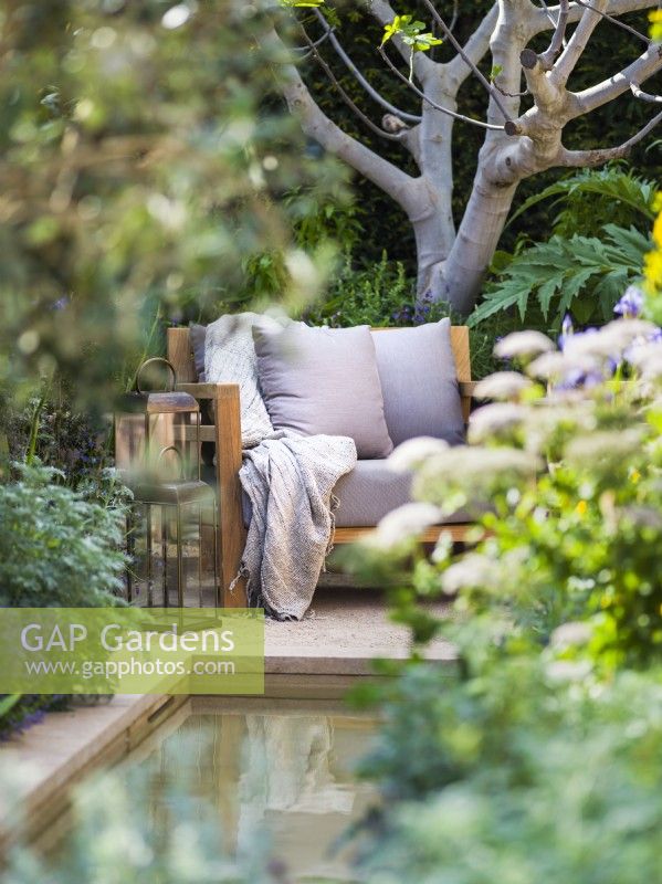 Secluded seating area with armchair and lanterns surrounded by Melanoselinum decipiens and architectural fig Ficus carica. Hamptons Mediterranean Garden, Designer: Filippo Dester Garden Club London, RHS Chelsea Flower Show 2023