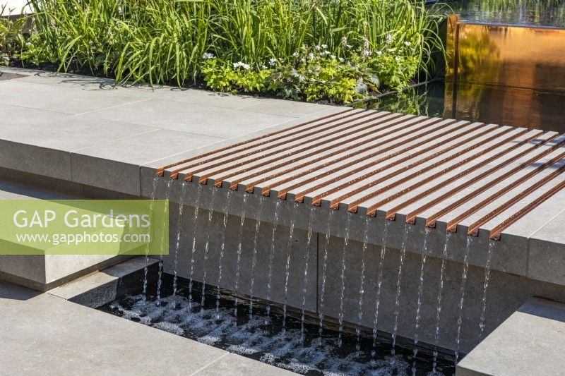 A water cascade of fluted copper grooves flows through the stone steps. Water flows down from the water feature located above.
