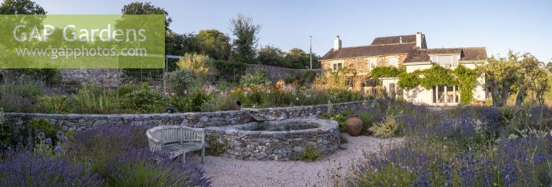 Small circular pond with stone sides in drought tolerant garden planted with Lavender, Verbena hastata and Heleniums.  The Walled Garden at Staverton, Devon