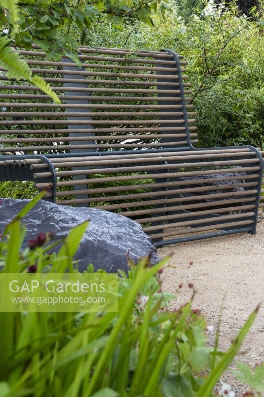A metal framed seat with wooden rods set among planting - Cancer Research UK Legacy Garden - designer Paul Hervey-Brookes - RHS Hampton Court Flower Palace Garden Festival 2023.