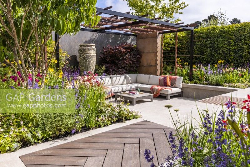 Contemporary garden with secluded seating area, steel pergola, walking board and large ceramic pot. Flower beds planted with Acer palmatum, Heptacodium and coloured perennials. June, Designer: Kevin Dennis, Bord Bia Bloom 2023