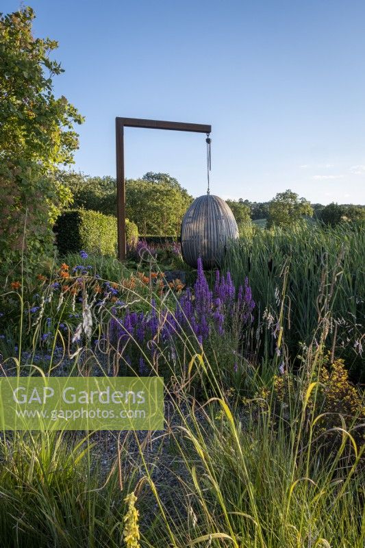 The steam bent oak 'egg' seat from Chelsea Flower Show 2021 takes centre stage in the dry garden at Holt Farm Gardens, Somerset