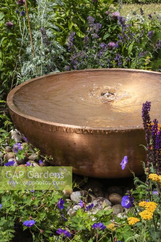 Circular copper water feature with bubble fountain. Planting includes Geranium 'Rozanne' and achillea. Designer Penelope Hill Smith - The Wilton London Botanical Fragrance Garden - RHS Hampton Court Palace Garden Festival.