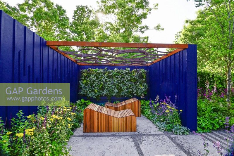 Relaxation area surrounded by a navy blue painted panels with decorative wooden deckchairs set against living green wall under with geometric design openwork of pergola roof. June
Bord Bia Bloom, Dublin
Designer: Jane McCorkell



