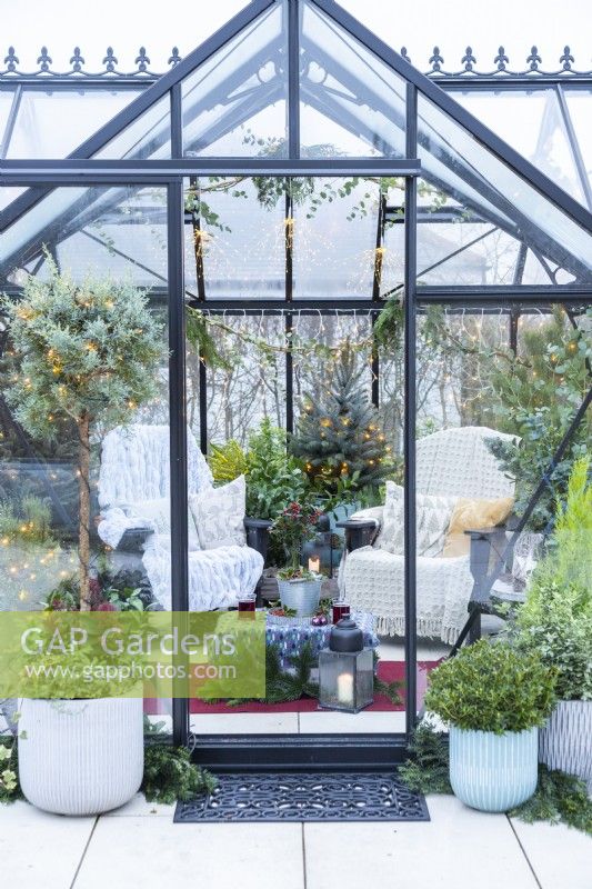 Large greenhouse furnished and decorated with recycled plastic chairs, fairy lights and mixed planting