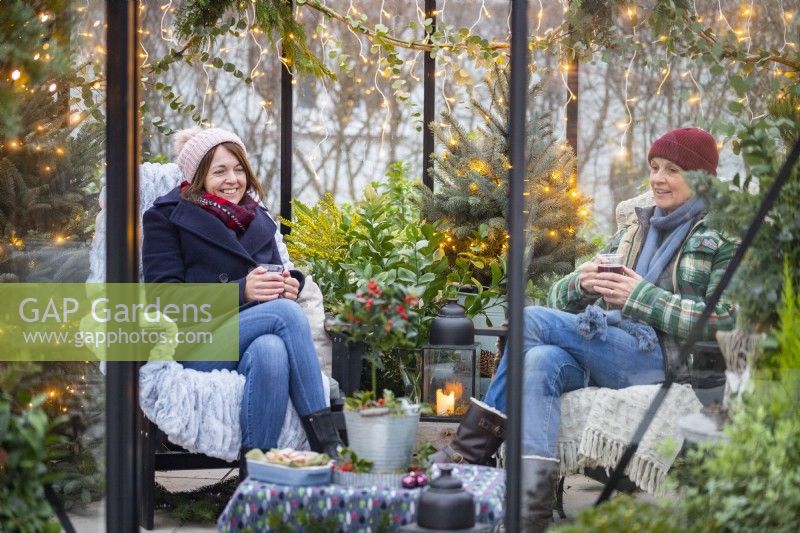 Women sitting in greenhouse with hot drinks, talking