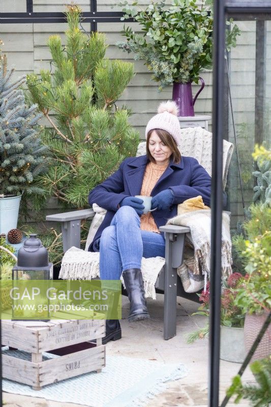 Woman sitting on chair with hot drink inside decorated greenhouse