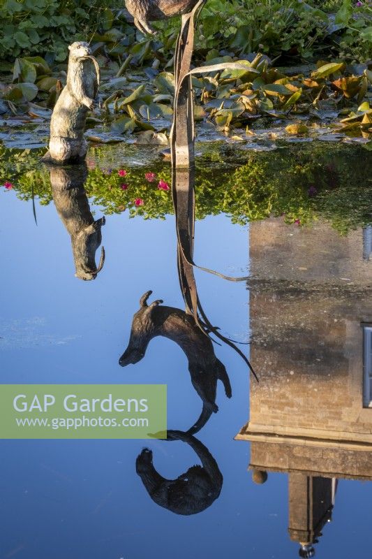 Ornamental sculptures of otters by Susie Wilson frolic above a formal pond which mirrors the surrounding formal garden.