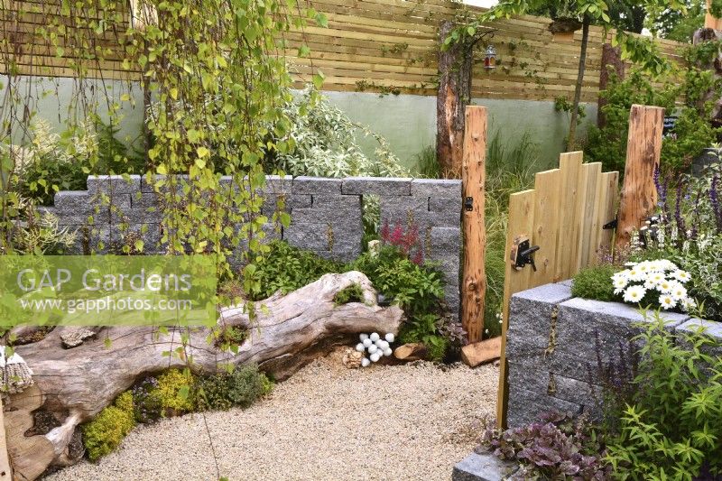 View a woodland inspired garden with a large tree stump lying on a gravel surface used as a flowerbed and seating area next to a Connemara wall system. Planted with Thymus vulgaris, Heuchera 'Licorice', Astilbe koreana, fungi, sedum, grasses. June
Designer: Mary Anne Farenden. Bord Bia Bloom, Super Garden, Dublin, Ireland.


 