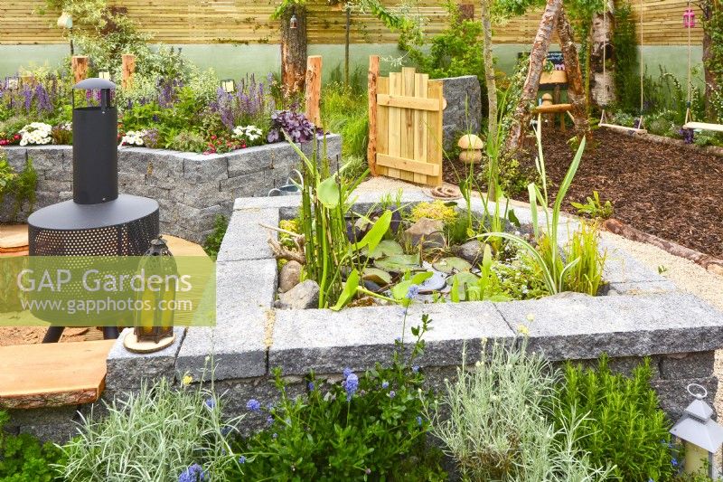 Mini raised pond with Connemara cap stones and picnic area with modern chiminea. Planted with Helichrysum italicum, Equisetum hyemale, aquatic plants in a woodland inspired garden. June
Designer: Mary Anne Farenden. Bord Bia Bloom, Super Garden, Dublin, Ireland.