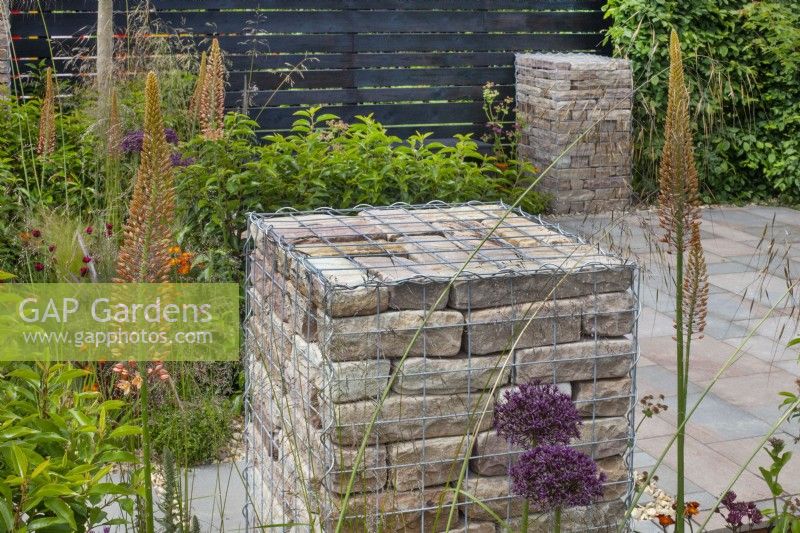 Brick filled gabions surrounded by perennials such as alliums, eremurus, and grasses in The 'Slow Burn' Garden at BBC Gardener's World Live 2015, June