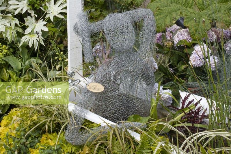 Wire female sculpture in a bath surrounded by foliage in the 'Recycled and Reused' garden at BBC Gardener's World Live 2015, June
