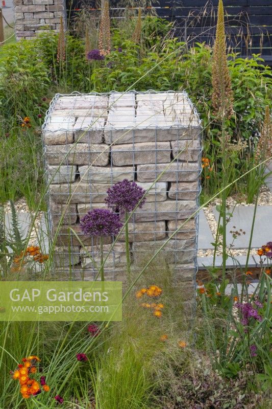 Brick filled gabion surrounded by perennials such as alliums, eremurus, and grasses in The 'Slow Burn' Garden at BBC Gardener's World Live 2015, June