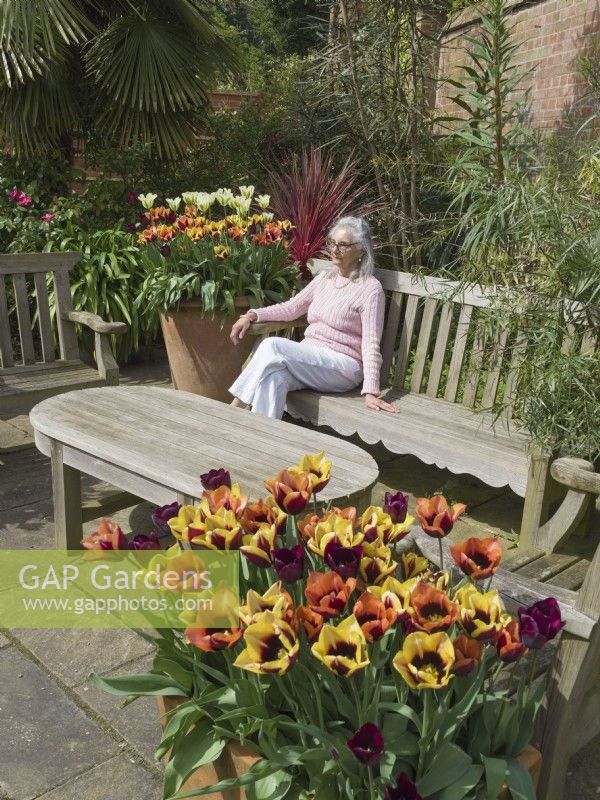 Woman sitting in seating area of garden with tulip planted containers