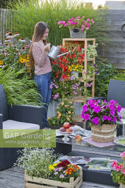 A woman watering bedding flowers in containers on a wooden flower stand.