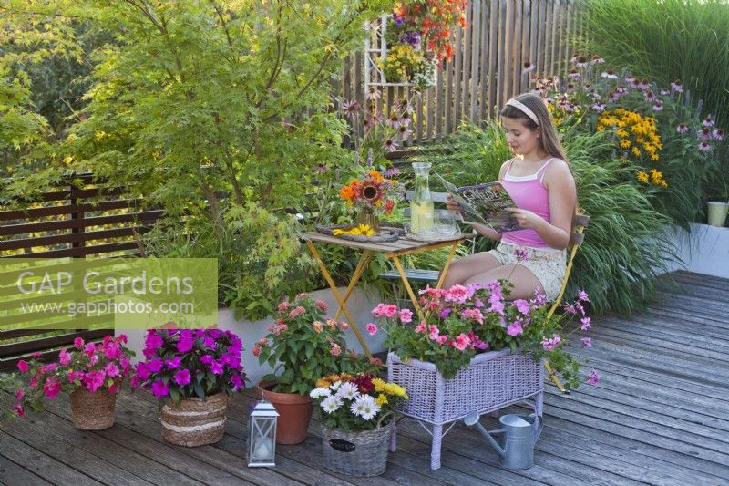Colourful summer terrace with bedding flowers in containers, a girl enjoys reading a magazine.