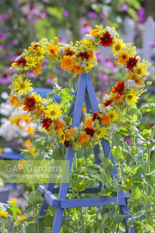 A wreath made of summer flowers including Helianthus, Coreopsis, Calendula, Foeniculum and Achillea on top of wooden obelisk.