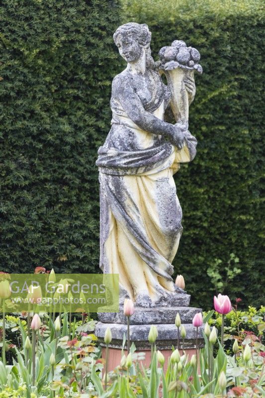 Classical statue of woman carrying basket of flowers. April. Spring.