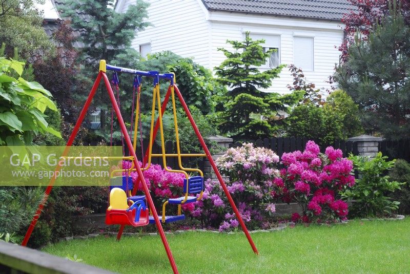 Colorful childrens swing  on a lawn in spring garden with Azaleas.