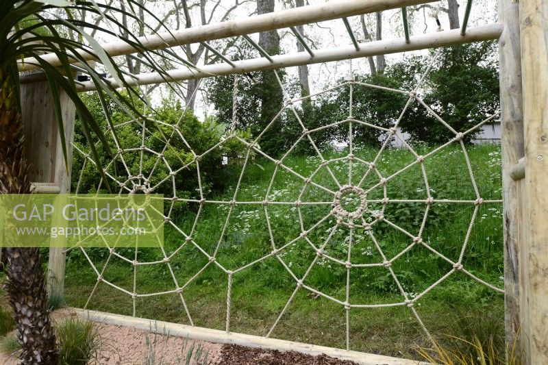 Climbing frame shaped like a spider's web made out of rope with wooden frame. May