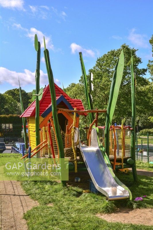 Colorful wooden playhouse with slide in the playground on lawn in garden. September