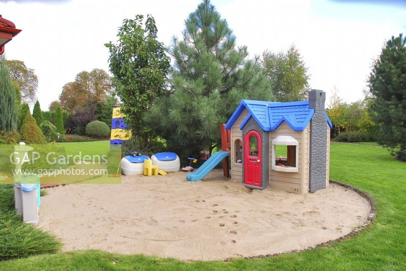 A playground for small children in a circular sandpit in summer garden.