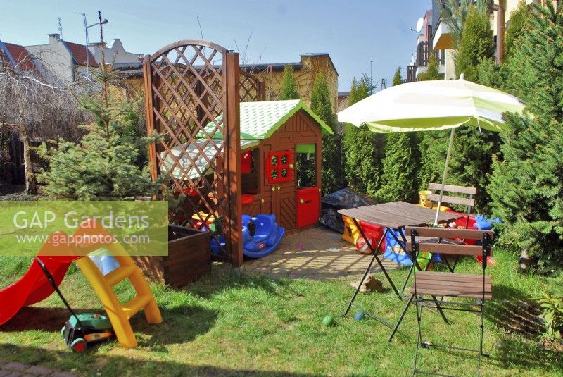 A playground for small children, fenced with openwork panels, with a wendy house in the garden in spring urban garden.