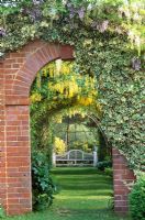 Brick arch with varigated Hedera - Ivy and Wisteria, view to Laburnum pergola and bench at Selehurst in Sussex