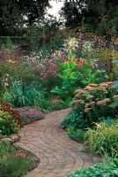 Curvy brick path between borders with Nicotiana sylvestris and Sedums at Pannells Ash Farm in Essex