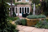 Urban garden with raised bed, paving and seating area by house