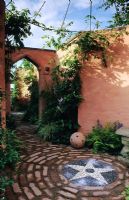 Colour washed walled patio with mosaic paving and trompe loeil in mirror in arched doorway