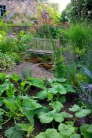 Wooden bench in informal bed with view to vegetable garden at Lower House, Powys in Wales