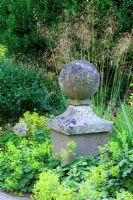 Stone sphere in informal border with Alchemilla mollis and Stipa at Lower House, Powys in Wales